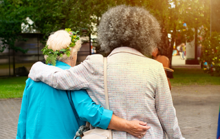 An elderly queer couple walking with arms linked. There is a pride flag next to them.