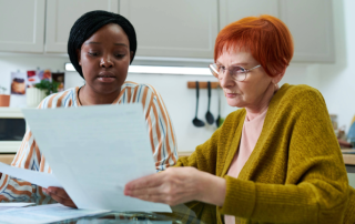 Private caregiver assisting elderly woman with paperwork.