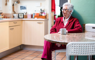 Elderly woman sitting at her kitchen table with a cup of coffee.