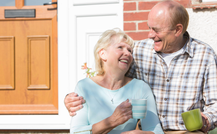 Elderly couple holding each other in front of their home.